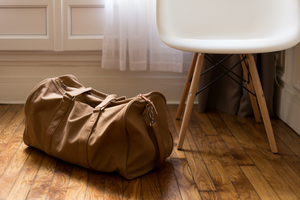 brown duffle bag on wooden floor next to a white chair