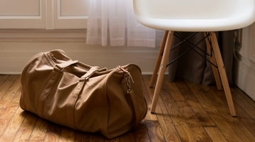  brown duffle bag on wooden floor next to a white chair